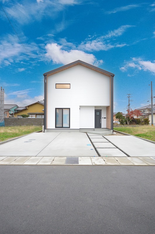 青空に映える白い外観、スタイリッシュな切妻屋根が印象的な二階建て住宅